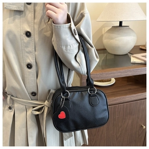 Detail of black litchi grain handbag featuring round metal handles and red heart charm