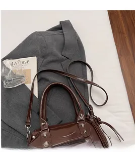 Dettaglio borsa Boston marrone scuro lucida con borchie su un blazer grigio