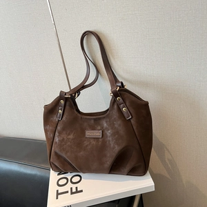Deep brown matte leather tote bag with rivet details displayed on a white fashion book