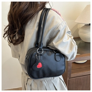 Détail d'un sac à main noir en cuir grainé avec un pendentif en forme de cœur rouge