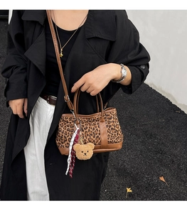 Leopard print canvas shoulder bag with plush bear charm worn by a model in black coat