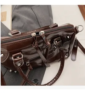 Dettaglio delle doppie cerniere scorrevoli e borchie argentate sulla borsa marrone