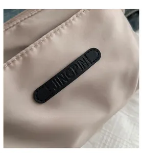 Macro detail of beige water-resistant nylon fabric and black leather logo patch on bag