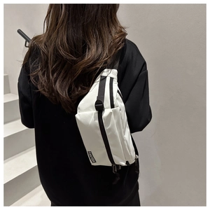 Detail of white nylon crossbody bag with wide black strap on model, minimalist streetwear