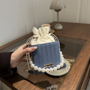 Blue woven bucket bag with pearl handle and gold chain strap shown in indoor setting