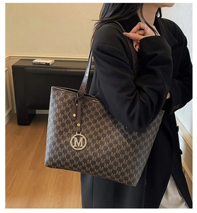 Detail of large tote bag with brown M-pattern and gold charm worn with a black blazer