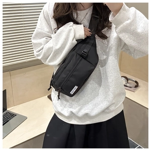 Close-up of black crossbody chest bag with minimalist white brand label and zipper