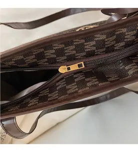 Close-up of a smooth gold metal zipper on a brown jacquard tote bag for women