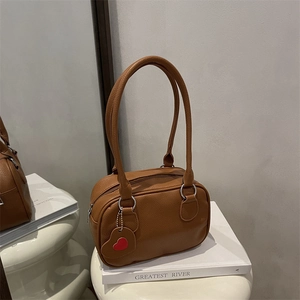 Sac à main en similicuir marron avec pendentif cœur rouge posé sur un livre blanc