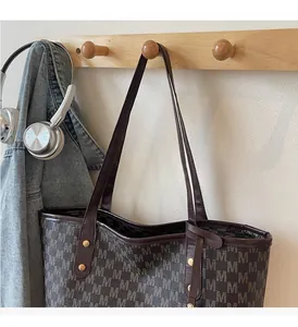 Detail of printed tote bag with brown leather trim and gold studs on a wooden rack