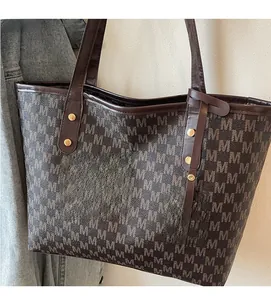 Detail of coffee tote bag with M-pattern monogram, leather handle, and gold metal charm