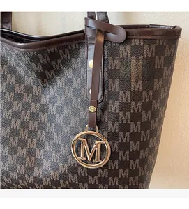 Detail of brown tote bag with M letter pattern and gold metallic letter charm