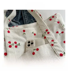 Détail du sac cabas en velours côtelé blanc avec broderie cerise et poche avant