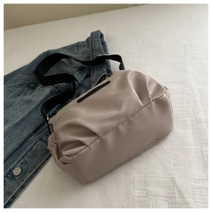 Detail shot of beige nylon crossbody bag with pleated design on blue denim jacket