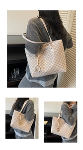 Detailed view of cream tote bag with repetitive dark letter print and metal charm