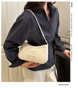 Detail view of cream leather underarm bag with embossed logo worn by a model