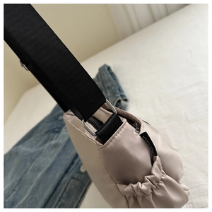 Detail view of beige nylon crossbody bag featuring a drawstring side pocket and logo