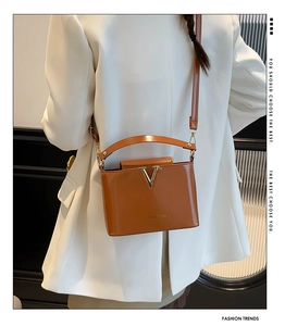 Close-up of a brown leather crossbody bag with a gold V logo on a model in a white blazer