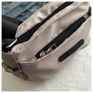 Close-up of beige nylon crossbody bag featuring multi-layer zippers and brand logo