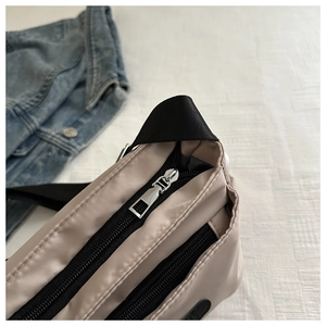 Close-up of beige nylon crossbody bag featuring multi-layer silver zippers and black straps