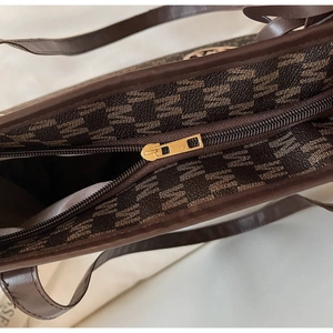 Detailed close-up of premium gold zipper closure on brown monogram tote bag with leather trim