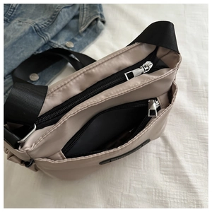Detail view of large beige nylon multi-layer crossbody bag with wide black strap