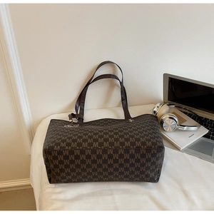 Detailed view of brown tote bag with M-pattern print near a laptop and headphones