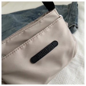 Detail of light beige nylon crossbody bag with black JINGPIN patch on white quilted fabric