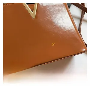 Close-up of brown glossy leather handbag featuring a golden V-shaped metal hardware detail