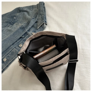 Detail of light beige crossbody bag showing spacious interior with wallet and accessories