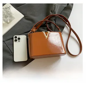 Detail view of a brown glossy leather crossbody bag with golden V hardware and text detail