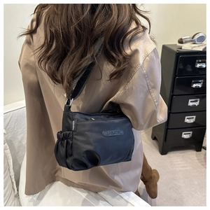 Detail view of black nylon crossbody bag with multi-pocket zippers and elastic side pocket