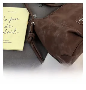 Detail of dark brown suede shoulder bag featuring decorative drawstring knot and metal rings
