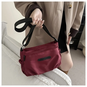Detail of burgundy nylon crossbody bag with adjustable strap and brand logo label