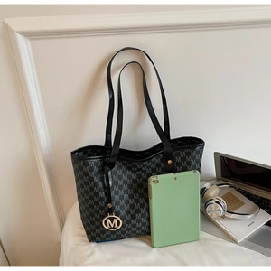 Macro shot of black tote bag with M-pattern print and gold logo charm on white surface