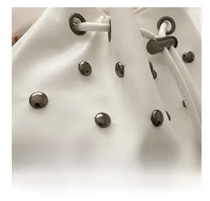 Close-up of white soft leather bucket bag featuring vintage silver studs and drawstring