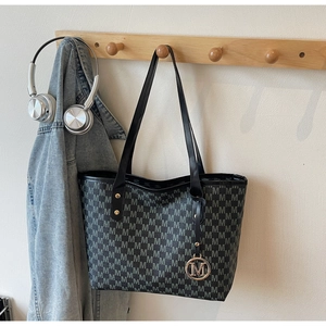 Detail of a large tote bag with M-pattern texture and gold metal pendant on a wooden hook
