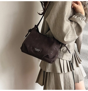 Detail of dark brown suede shoulder bag with stylish knot strap and logo plaque