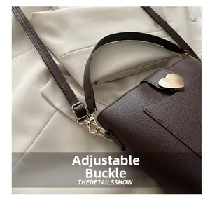 Detail of adjustable strap buckle and golden heart metal buckle on brown leather bag