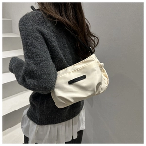 Detail of a creamy white shoulder bag with side pleats and black adjustable strap