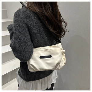 Detail of cream nylon shoulder bag featuring side pleats and black branded logo plate