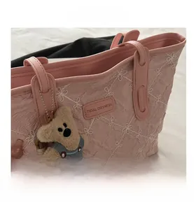 Detailed close-up of pink tote bag with white floral embroidery and cute bear charm