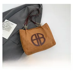 Detalle de bolso tote de ante marrón con logotipo HB de cuero y cadena dorada