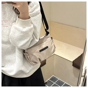 Detail view of beige nylon crossbody bag with black adjustable strap and logo patch