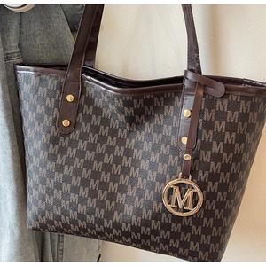 Detailed close-up of dark brown tote bag with M-letter monogram and gold metal charm