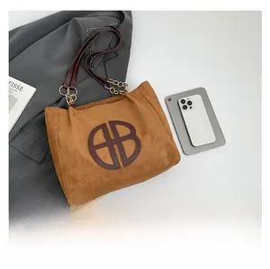 Primer plano del bolso tote de ante marrón con correa de cuero y logotipo HB en mesa