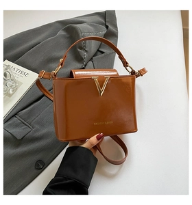Detail of a brown leather bag with a gold V-shaped logo on a stylish office background