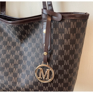 Detail of monogram M pattern and gold metal logo pendant on a brown tote bag