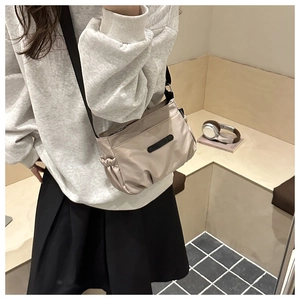 Detail of champagne nylon crossbody bag showing side pleats and contrast black strap