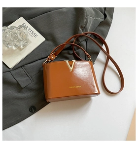 Detailed view of caramel brown leather handbag with metal V-notch on grey blazer